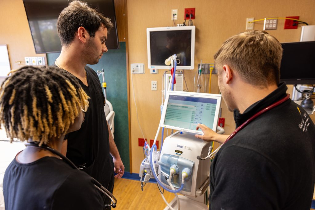 Three healthcare providers gather around a piece of medical equipment.